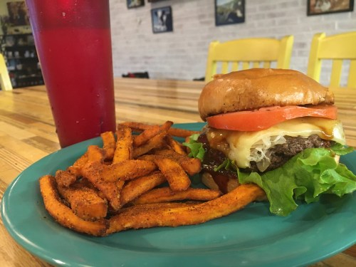A juicy burger with lettuce, tomato, and cheese, served with sweet potato fries and a red drink on a blue plate.
