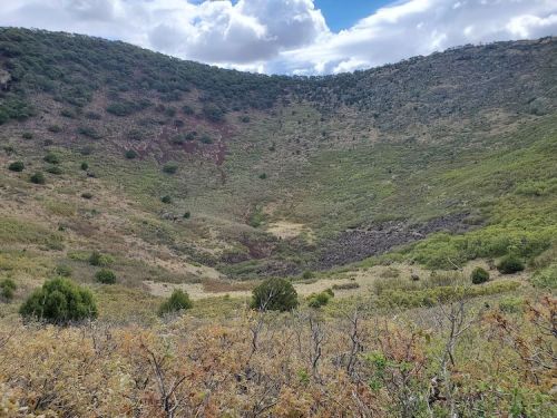 A lush, green volcanic crater surrounded by hills under a partly cloudy sky.