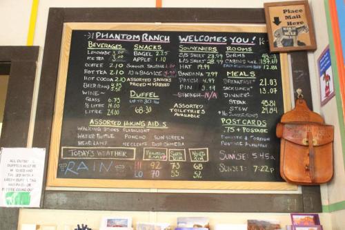 Menu board at Phantom Ranch displaying beverages, snacks, souvenirs, rooms, meals, weather, and sunset time.