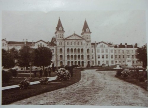 Historic building with twin towers, surrounded by trees and a pathway, captured in sepia tones.