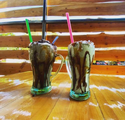 Two tall glasses of chocolate milkshakes with whipped cream and colorful straws, set on a wooden table.