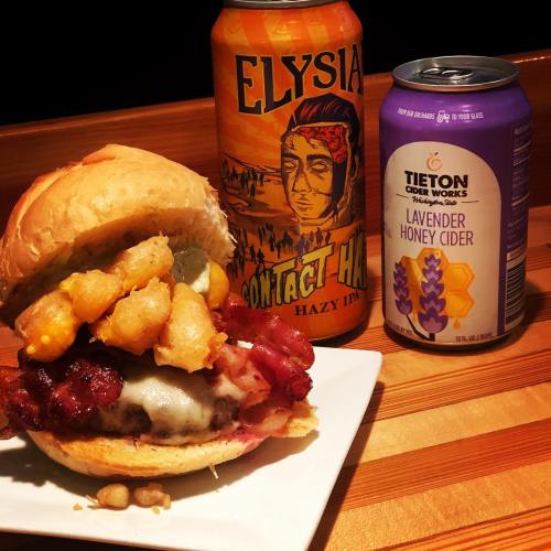 A hearty burger topped with bacon and tater tots, accompanied by Elysia Hazy IPA and Tieton Lavender Honey Cider.