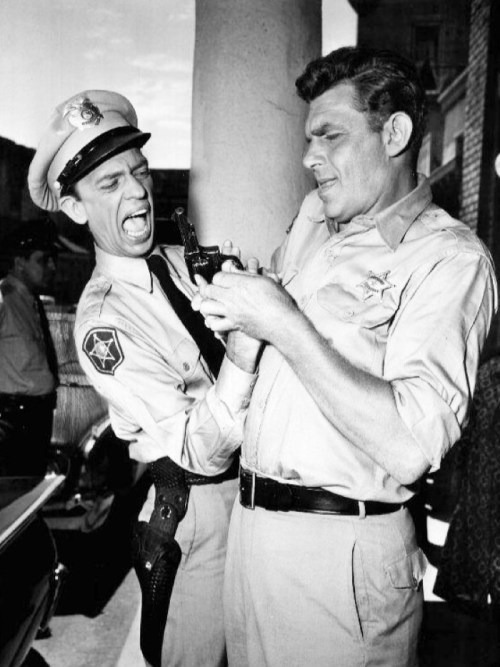 Two police officers struggle over a revolver, showcasing a tense moment in a vintage black-and-white scene.