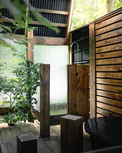 Outdoor shower surrounded by wooden walls and greenery, with natural light filtering through.