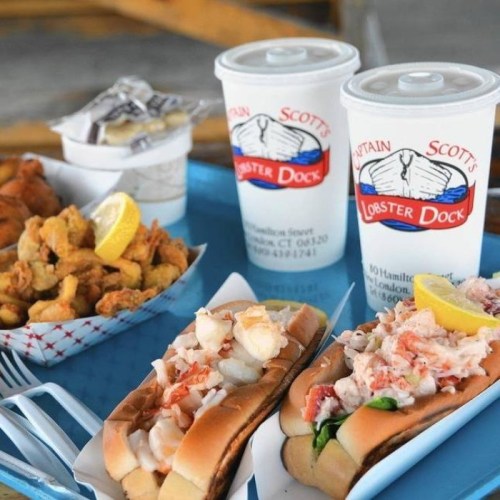 A tray with lobster rolls, fried clams, and two drinks from Captain Scott's Lobster Dock.