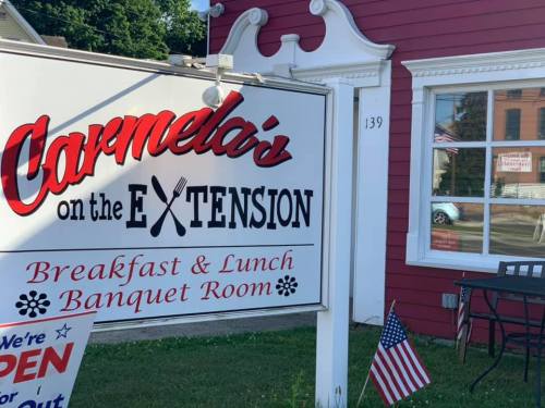 Sign for "Carmela's on the Extension," a breakfast and lunch restaurant with a banquet room, featuring an American flag.