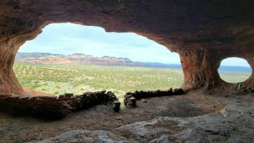 View from inside a cave, showcasing a scenic landscape with mountains and greenery through two openings.