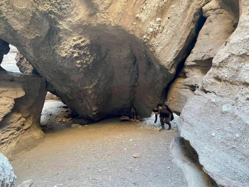 A person exploring a narrow canyon with large rock formations and sandy ground.