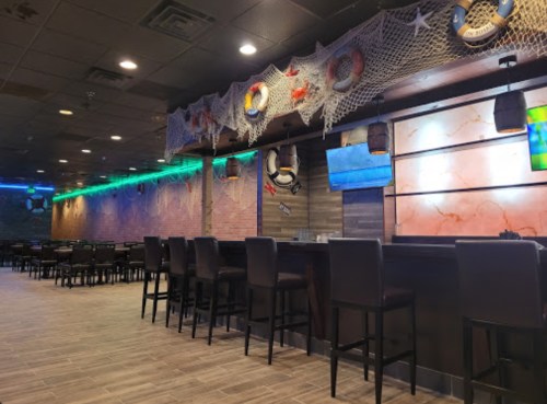Interior of a bar with nautical decor, featuring a long counter, high chairs, and colorful lighting.