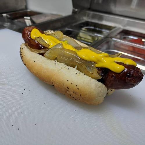 A poppy seed hot dog bun filled with a grilled sausage, topped with sautéed onions and yellow mustard.