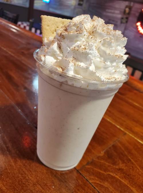 A tall cup of creamy milkshake topped with whipped cream and a sprinkle of cinnamon, garnished with a cookie.