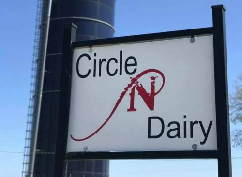 A black silo with an American flag and a sign reading "Circle N Dairy" in front, set against a clear blue sky.