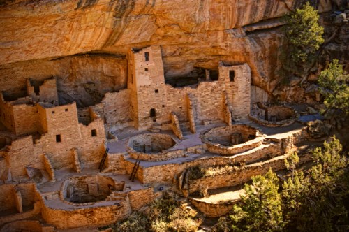 Ancient stone ruins nestled in a rocky cliff, surrounded by trees and natural landscape.