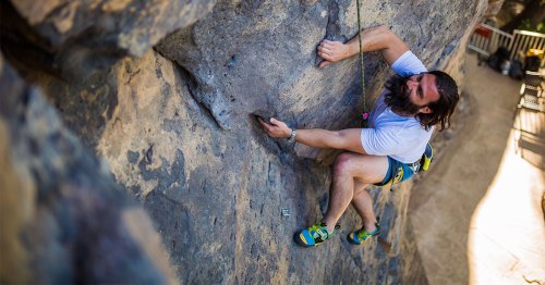 A climber ascends a rocky wall, gripping a handhold with determination, wearing climbing shoes and a harness.