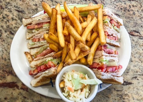 A plate with a stacked turkey sandwich, fresh tomatoes, lettuce, crispy fries, and a small bowl of coleslaw.