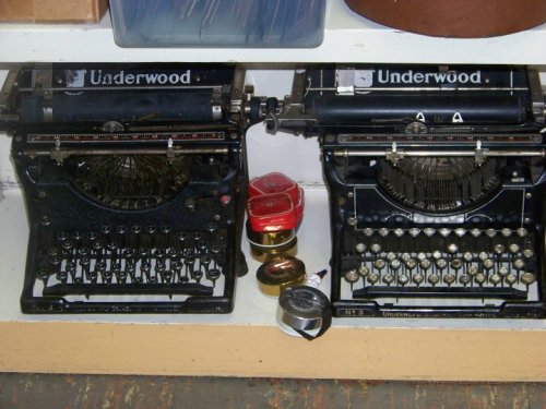 Two vintage Underwood typewriters on a shelf, with small tins and a roll of tape nearby.