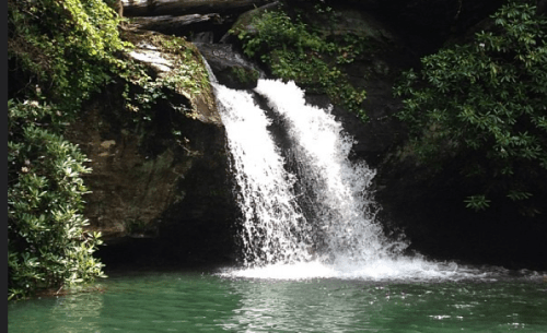 A serene waterfall cascading into a clear pool, surrounded by lush greenery and rocky cliffs.
