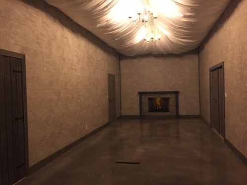 A spacious, empty room with textured walls, a chandelier, and a fireplace, featuring two closed doors on opposite walls.