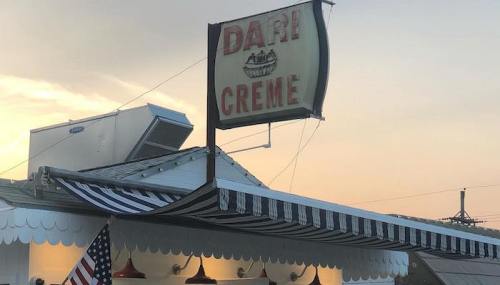 Sign for "Dari Creme" ice cream shop with a vintage design, featuring red accents and an American flag.