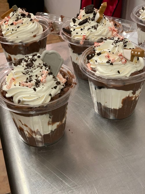 Delicious chocolate desserts in clear cups, topped with whipped cream, crushed cookies, and festive candy pieces.