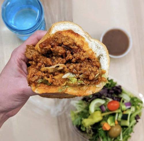 A hand holding a large fried chicken sandwich with lettuce, alongside a salad and a glass of water.