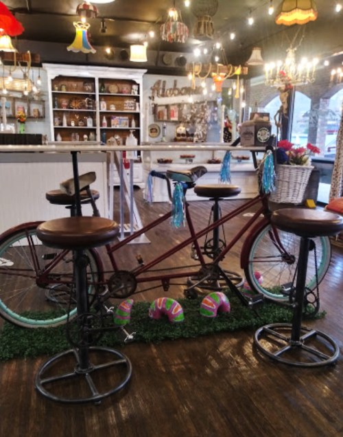 A vintage tandem bicycle with bar stools, decorated with colorful tassels, set in a cozy, eclectic café interior.