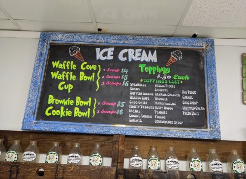 Chalkboard menu displaying ice cream options, prices, and toppings at an ice cream shop.