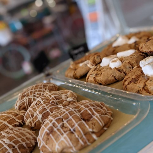 A display of freshly baked cookies, one variety drizzled with icing and the other topped with marshmallows.