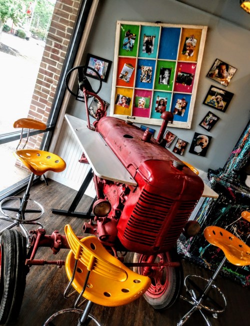 A vintage red tractor converted into a table, surrounded by yellow stools and colorful framed photos on the wall.