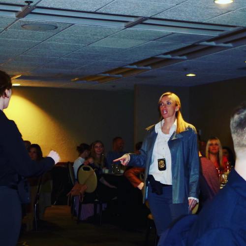 A woman in a police uniform gestures while speaking to another person in a dimly lit banquet room.