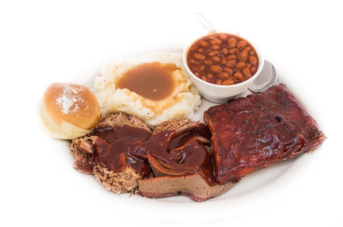 A plate of barbecue featuring pulled pork, ribs, mashed potatoes with gravy, baked beans, and a roll.