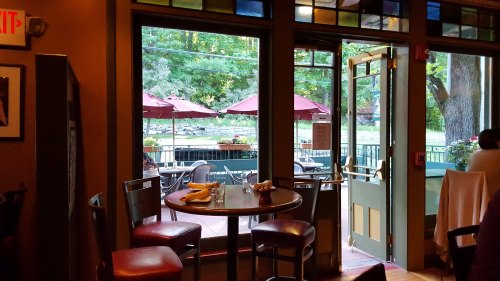 View from inside a restaurant, showing an open door and outdoor seating with umbrellas in a scenic setting.