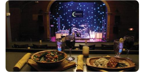 A dining table with two plates of food and drinks, overlooking a stage with lights and musical instruments.