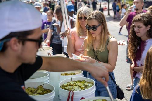 A busy outdoor market scene with people sampling pickles from buckets, enjoying the vibrant atmosphere.
