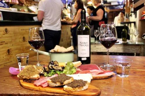 A table spread with wine, charcuterie, and bread, set in a lively restaurant atmosphere.