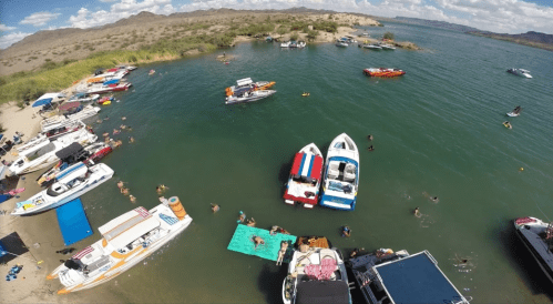 Aerial view of a busy lake with boats and people swimming, sunbathing, and enjoying the water on a sunny day.