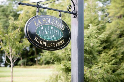 Sign for "La Soledad" in Harper's Ferry, featuring green and gold design, hanging from a black post.
