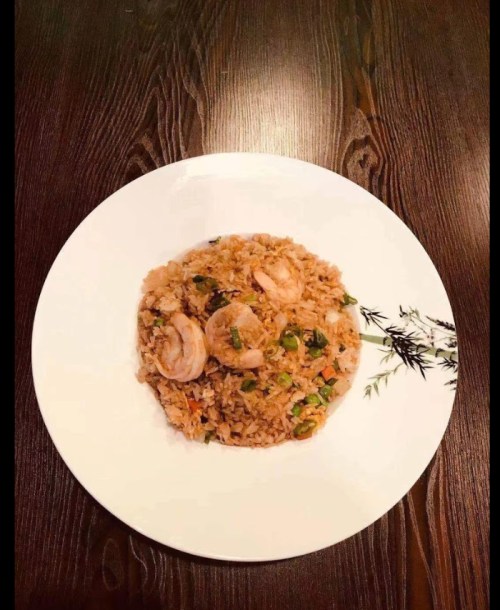 A plate of shrimp fried rice garnished with herbs, served on a wooden table.