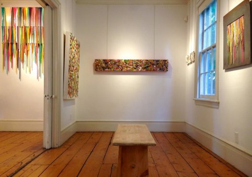 Art gallery interior featuring colorful abstract artworks on the walls and a wooden bench in the center.