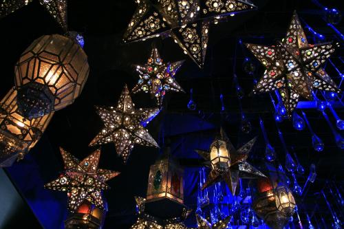 A collection of ornate, star-shaped lanterns hanging from the ceiling, illuminated with colorful lights against a dark background.