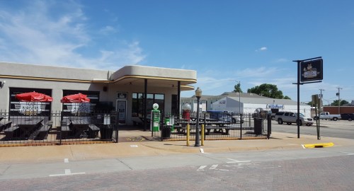 A fast-food restaurant with outdoor seating, red umbrellas, and a sign, set against a clear blue sky.
