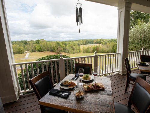 A dining table with gourmet dishes and wine, overlooking a scenic landscape of trees and rolling hills.