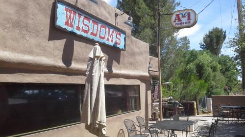Exterior of a rustic building with a sign reading "Wisdom's" and outdoor seating under a sunny sky.