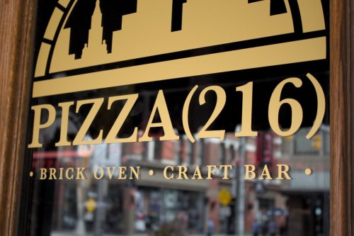 Sign for Pizza(216) featuring "Brick Oven Craft Bar" with a city skyline silhouette in the background.