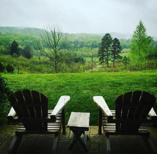 Two wooden chairs and a small table overlook a lush green landscape with rolling hills and trees under a cloudy sky.