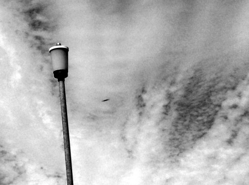 A tall streetlamp against a cloudy sky, captured in black and white.