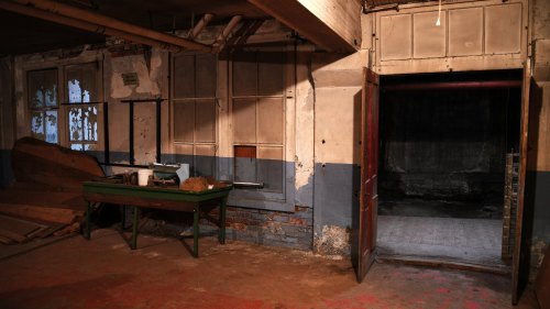 An empty, dimly lit room with peeling walls, a green workbench, and an open door leading to a dark space.