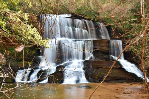 A serene waterfall cascading over rocks, surrounded by lush greenery and tree branches.