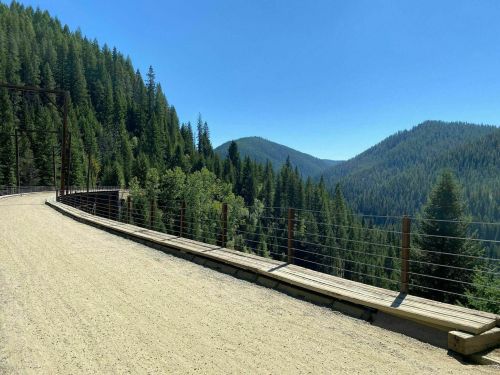 A scenic view of a gravel path along a forested mountain landscape under a clear blue sky.