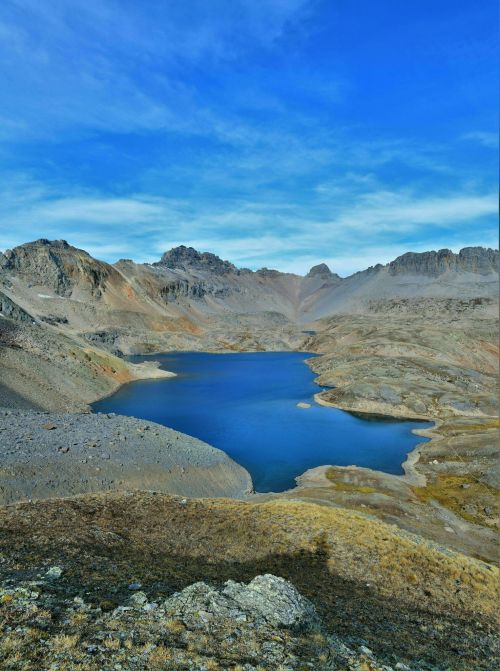 A serene mountain landscape featuring a blue lake surrounded by rocky terrain and distant peaks under a clear sky.